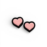 A pair of heart shaped wooden earrings painted pink with a black border.