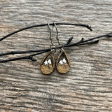 A pair of wooden earrings with mountain designs on them, resting on a wooden surface.