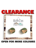 A pair of round wooden stud earrings displayed on a white card with the Birch Street Studio logo, framed by a rustic wood border. Large red text at the top reads 'CLEARANCE' and black text at the bottom reads 'OPEN FOR MORE COLOURS'.