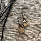 A pair of wooden earrings with a mountain design, resting on a wooden surface.