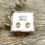 A pair of small wood studs earrings engraved with an image of geometric mountains.
