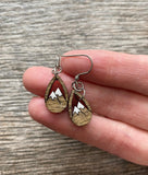 A hand holding a pair of wooden earrings with mountain designs on them.