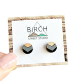 A pair of round wooden earrings with a black and grey chevron pattern.